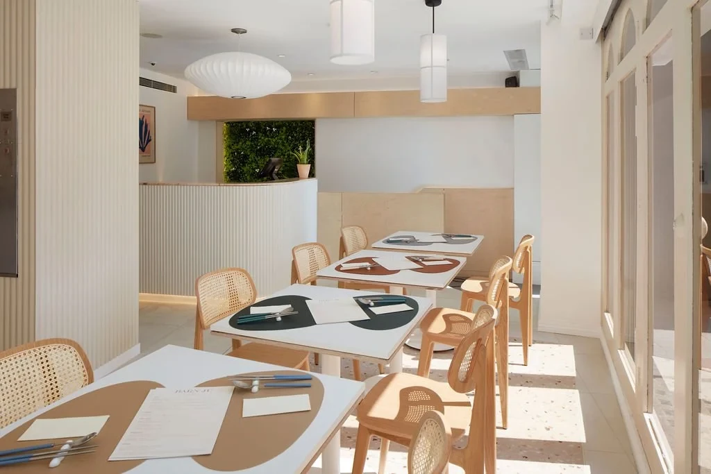 Barnju dining room with pale timber chairs, patterned tabletops and pendant lights beside the windows.