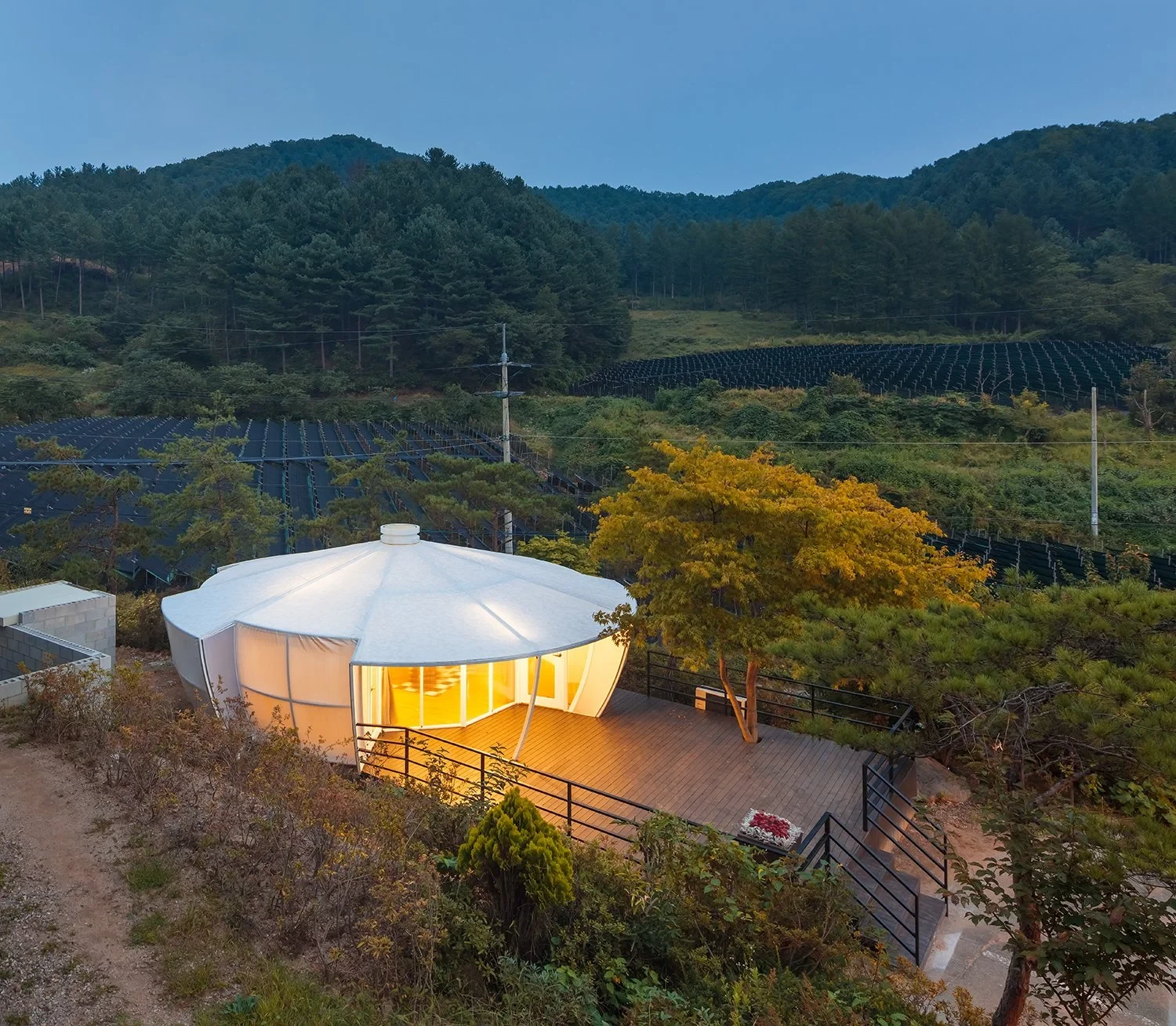 An illuminated glamping pod on a timber deck within a wooded hillside.